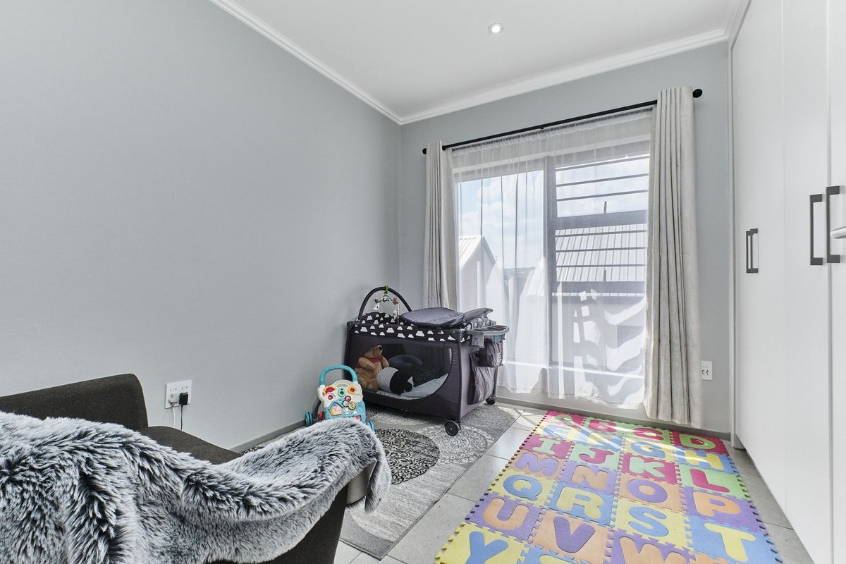 A bright bedroom featuring neutral walls, tiled flooring, built-in cupboards, and a sliding glass door providing access to the exterior.