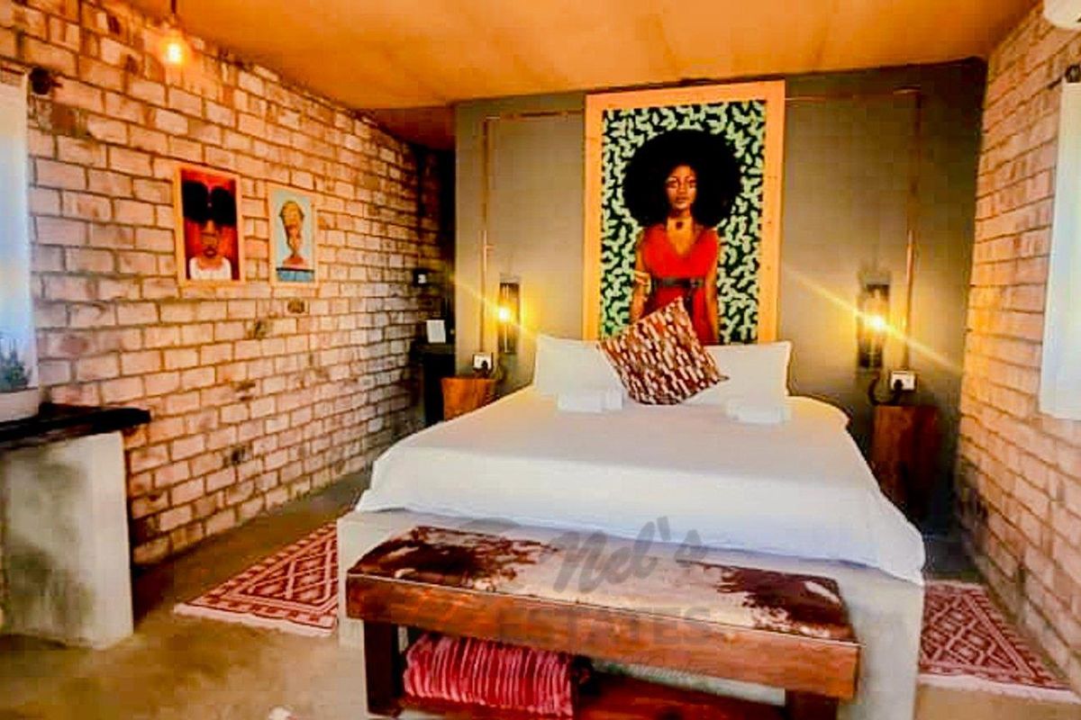 A rustic bedroom featuring exposed brick walls, a built-in concrete bedside shelf, and integrated wall lighting.