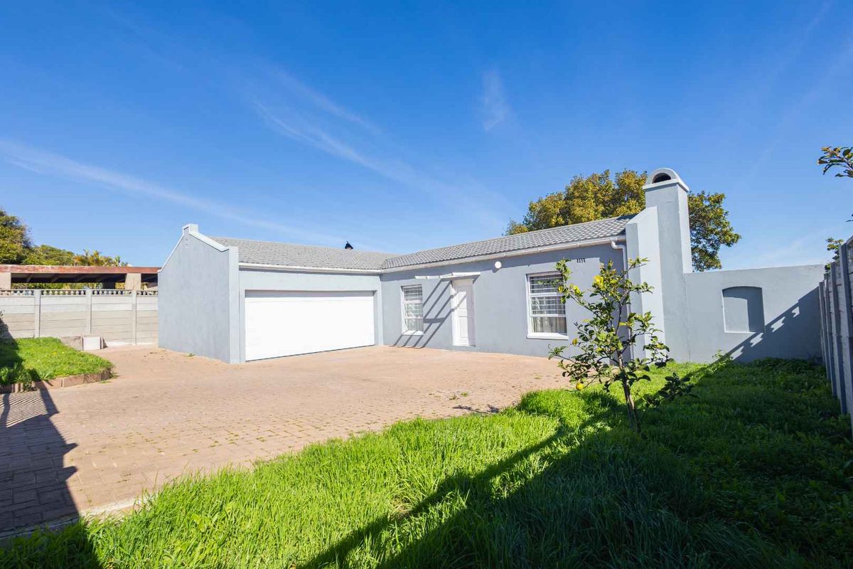 Rear view of the property featuring a paved driveway, attached garage, and a private garden area with boundary walling.