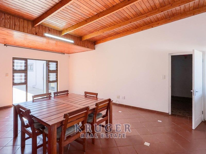 Open plan living area featuring exposed timber beam ceilings, terracotta tiled flooring, and direct access to an outdoor space through sliding glass doors.