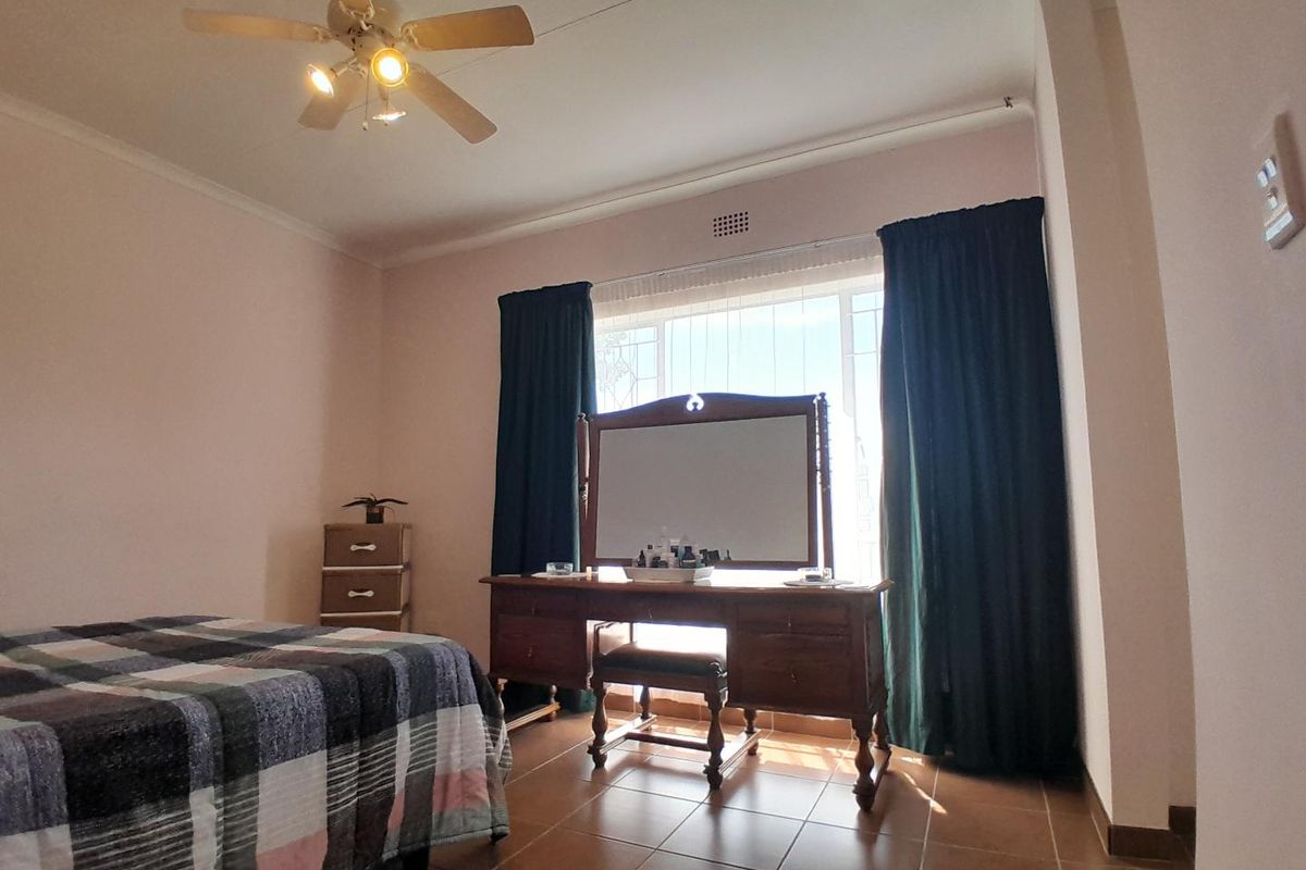 A bedroom featuring tiled flooring, a ceiling fan, and a large window with security bars, providing natural light.