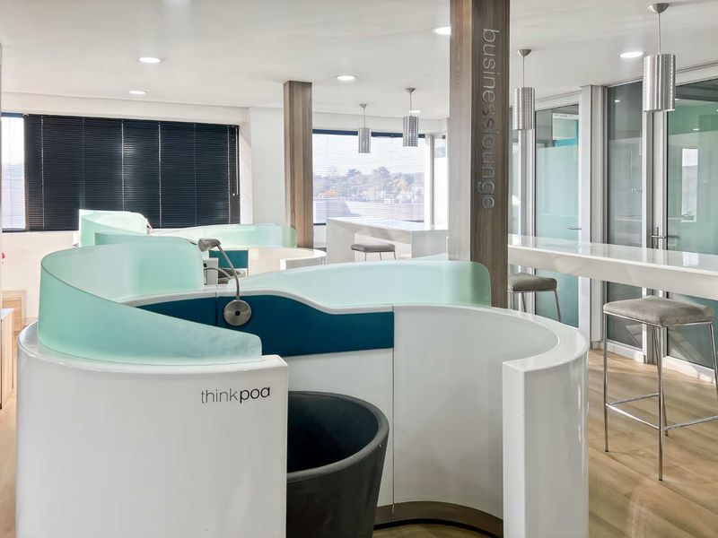 Modern office business lounge featuring curved privacy pods, integrated work counters, recessed lighting, and high-quality finishes throughout the professional workspace.