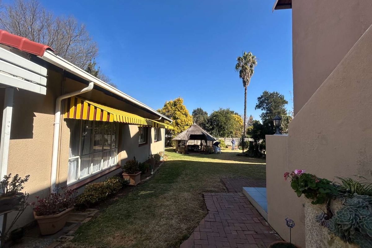 A rear garden view featuring a brick-paved walkway, a retractable awning over the house exterior, and a detached thatched gazebo in the backyard.