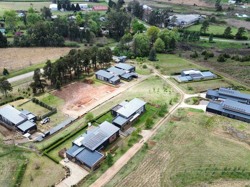 An aerial view of a residential estate featuring multiple modern homes with solar panels, paved driveways, and established garden landscaping.