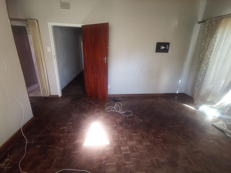 An empty bedroom featuring original parquet flooring, a wooden door, and neutral wall finishes, offering a blank canvas for renovation.