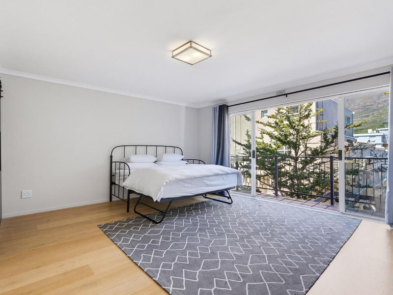 A bright bedroom featuring hardwood flooring, a sliding barn door, and large sliding glass doors that open onto a balcony with exterior views.