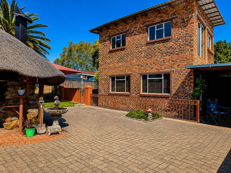 Rear view of a double-story face brick house featuring a paved courtyard and a traditional thatched lapa entertainment area.