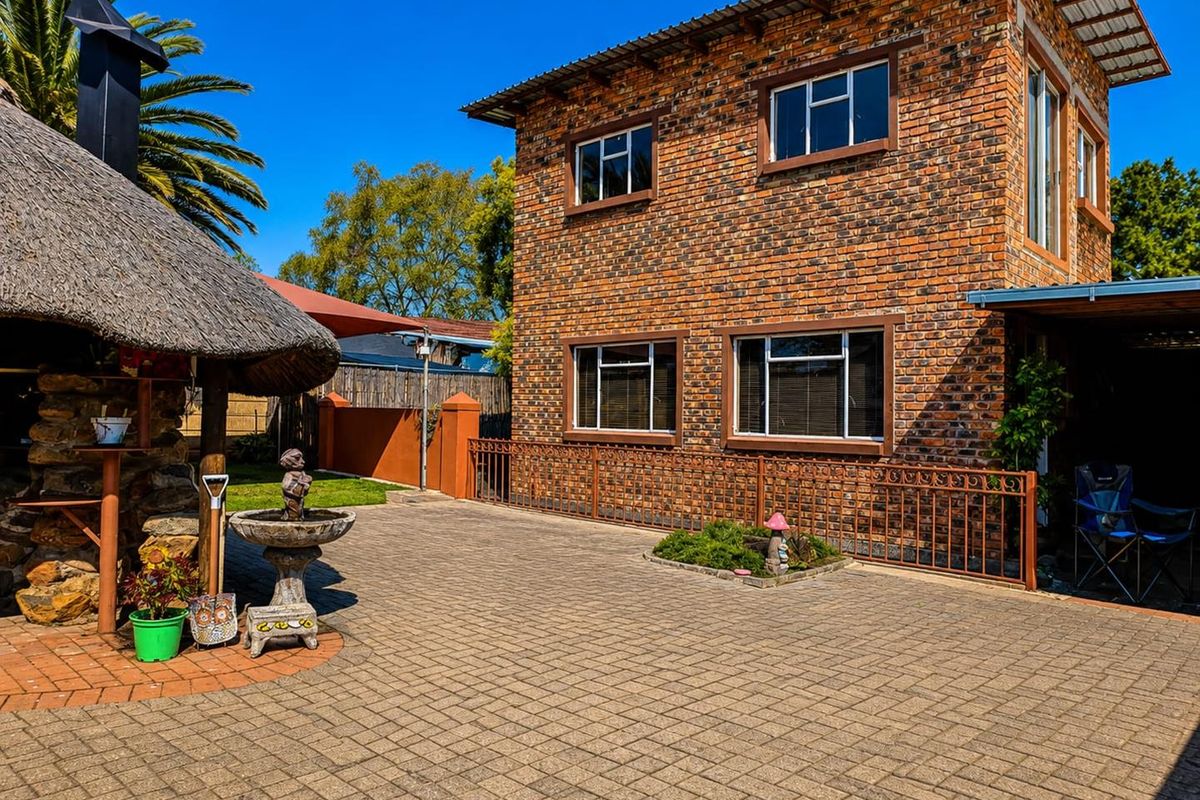 Rear view of a double-story face brick house featuring a paved courtyard and a traditional thatched lapa entertainment area.