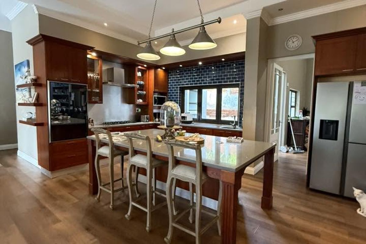 Spacious kitchen featuring a large central island with breakfast bar seating, dark wood cabinetry, subway tile backsplash, and integrated stainless steel appliances.