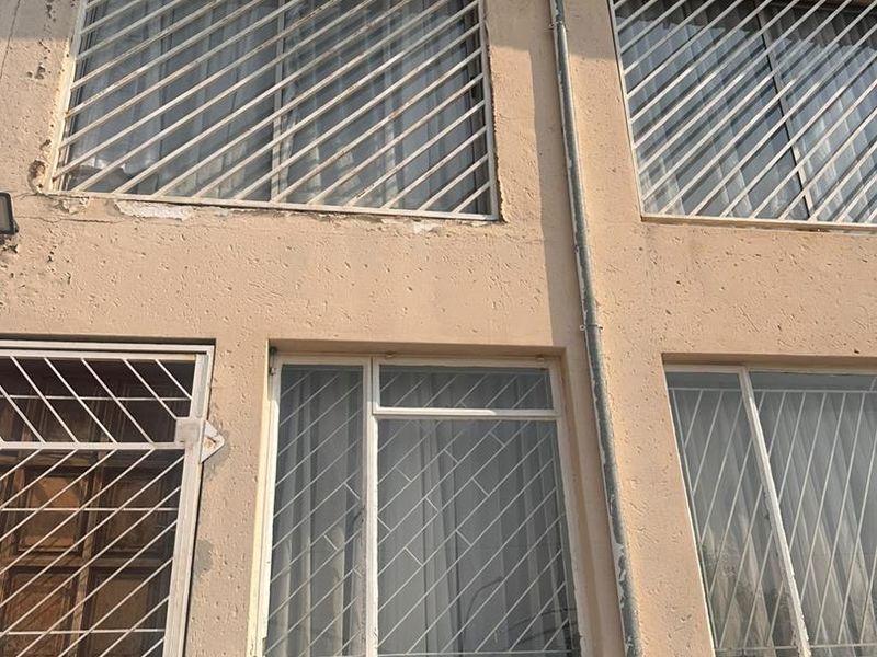 Front elevation of a townhouse featuring textured plaster walls, security bars on windows, and visible signs of exterior wear and paint deterioration.