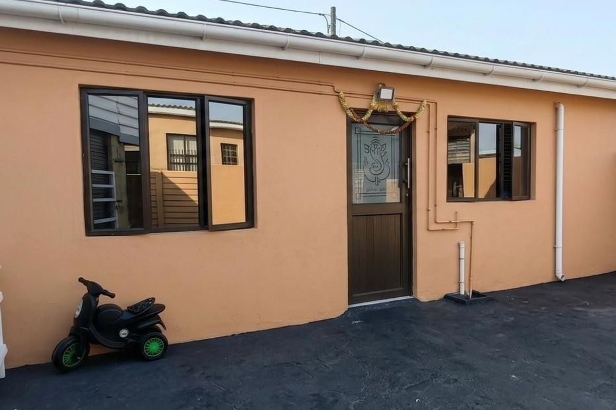 A well-maintained rear exterior view of the property featuring peach-toned rendered walls, dark aluminium window frames, and a paved outdoor area.