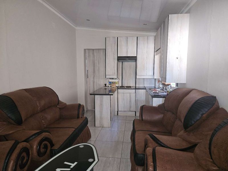 Open plan living area featuring a compact kitchen with built-in cabinetry, hob, extractor fan, and tiled flooring throughout.