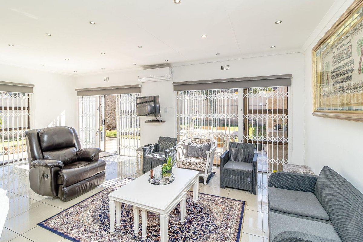 Bright and spacious living room featuring tiled flooring, recessed lighting, split-system air conditioning, and large sliding glass doors with security gates leading to the patio.