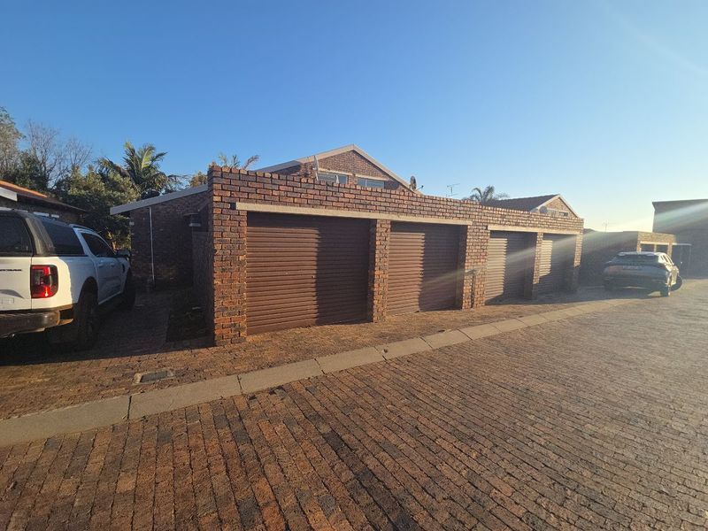 Exterior view of a townhouse property featuring a triple garage with roller shutter doors and a paved driveway.