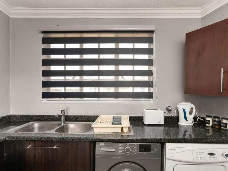 A functional kitchen area featuring dark wood cabinetry, granite countertops, and a double basin stainless steel sink with modern zebra blinds.