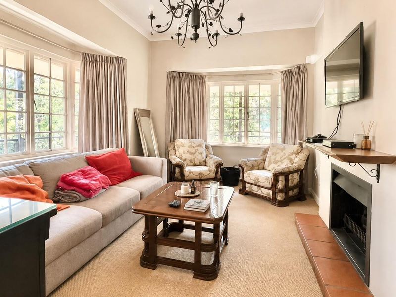 A comfortable living room featuring a fireplace with a tiled hearth, mantelpiece, and large bay windows that provide ample natural light.