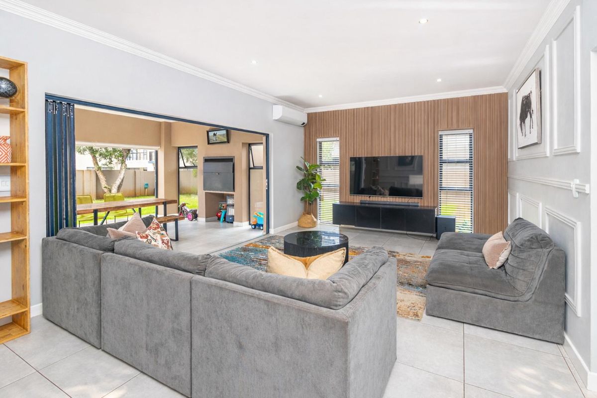 Modern living room featuring a timber slat feature wall, tiled flooring, and large stacking doors that open onto a covered patio area.