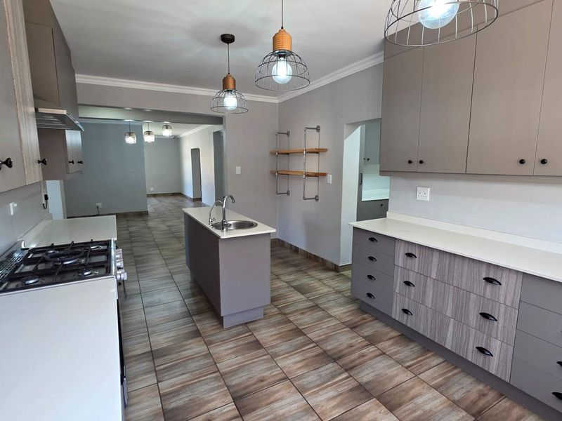 Modern kitchen featuring a central island with sink, gas hob, ample built-in cabinetry, stone countertops, and durable tiled flooring throughout.