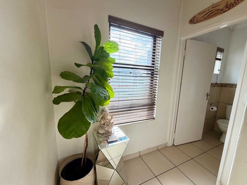 A bright hallway featuring tiled flooring and venetian blinds, providing access to an adjacent bathroom.