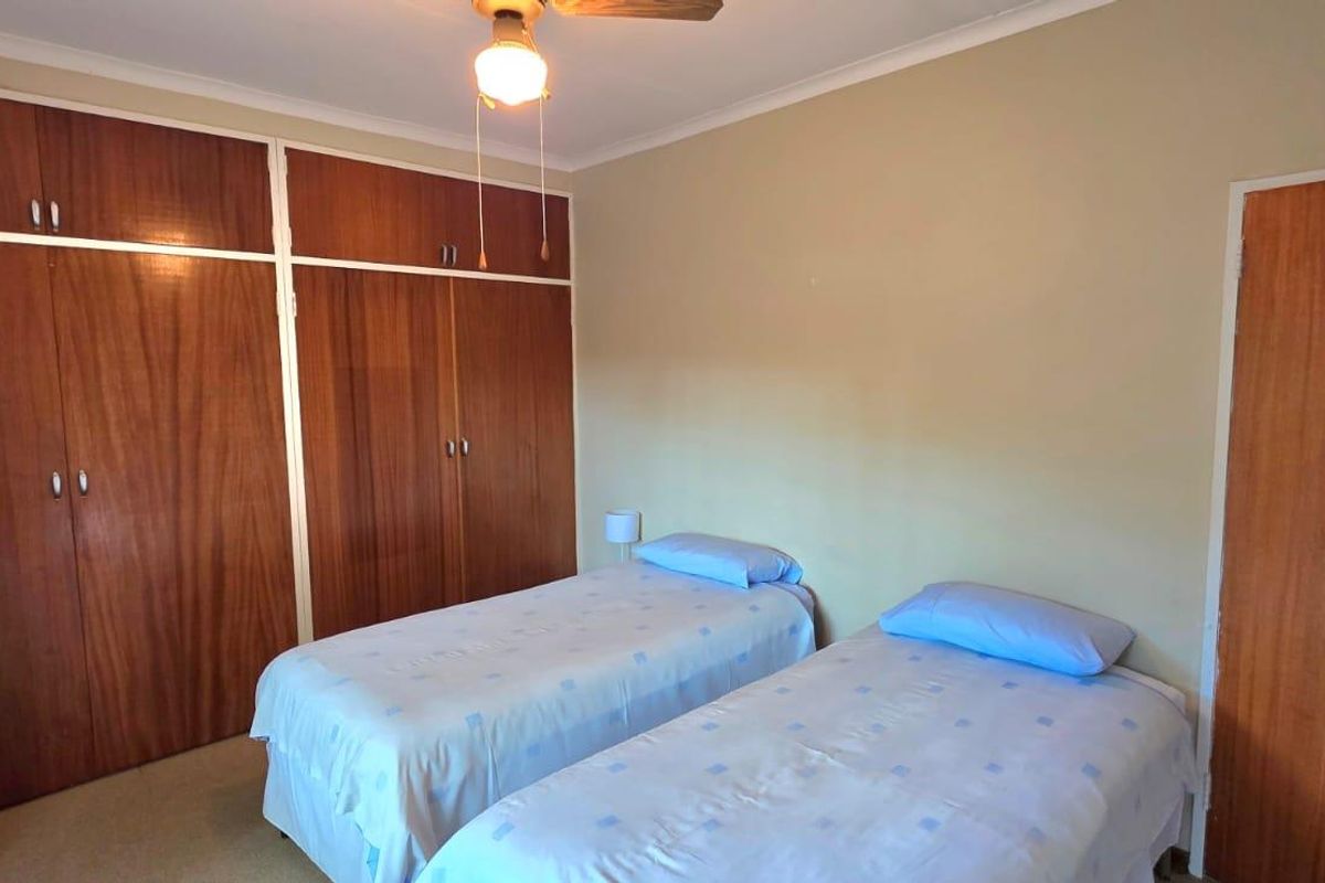 A bedroom featuring built-in wooden cupboards, a ceiling fan, and neutral wall finishes.