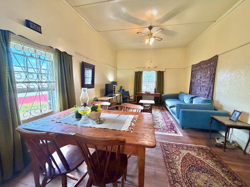 A living room featuring timber flooring, a ceiling fan, and security bars on the windows, with visible plaster cracks on the wall.