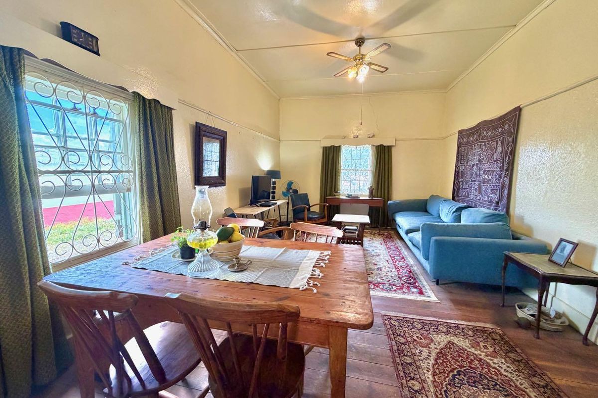 A living room featuring timber flooring, a ceiling fan, and security bars on the windows, with visible plaster cracks on the wall.