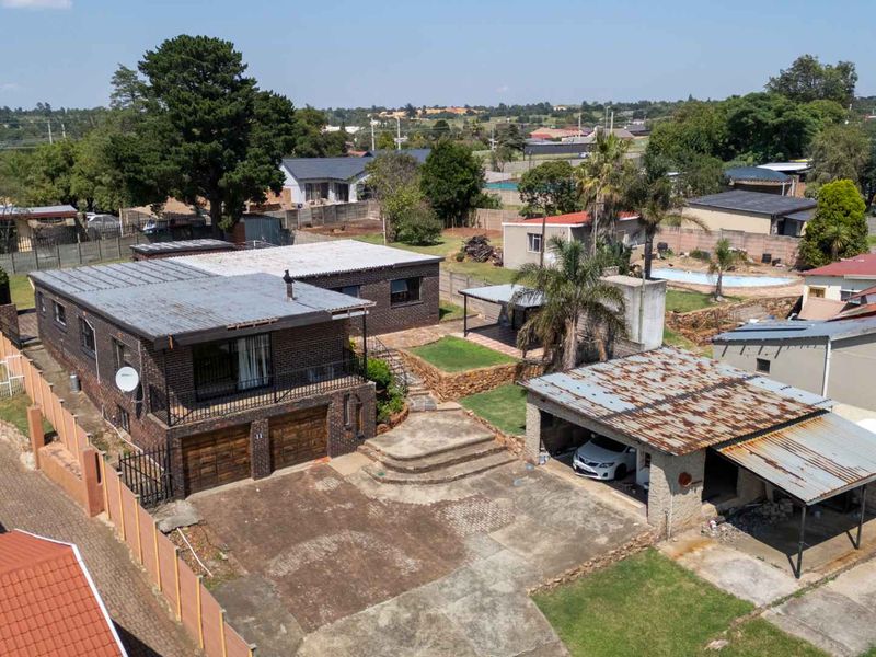 Aerial view of a residential property featuring a brick house, double garage, carport, and paved driveway within a suburban neighborhood setting.