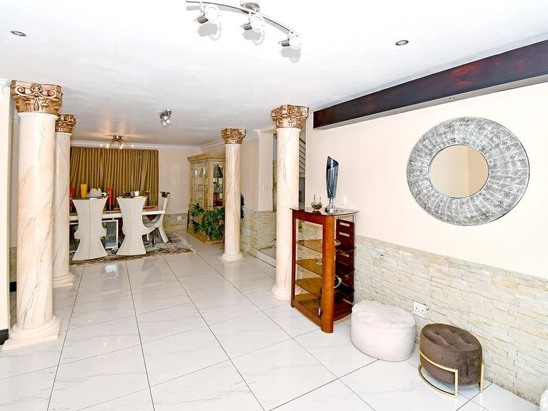 Spacious open-plan living and dining area featuring decorative columns, stone veneer wall accents, and polished porcelain floor tiles throughout.