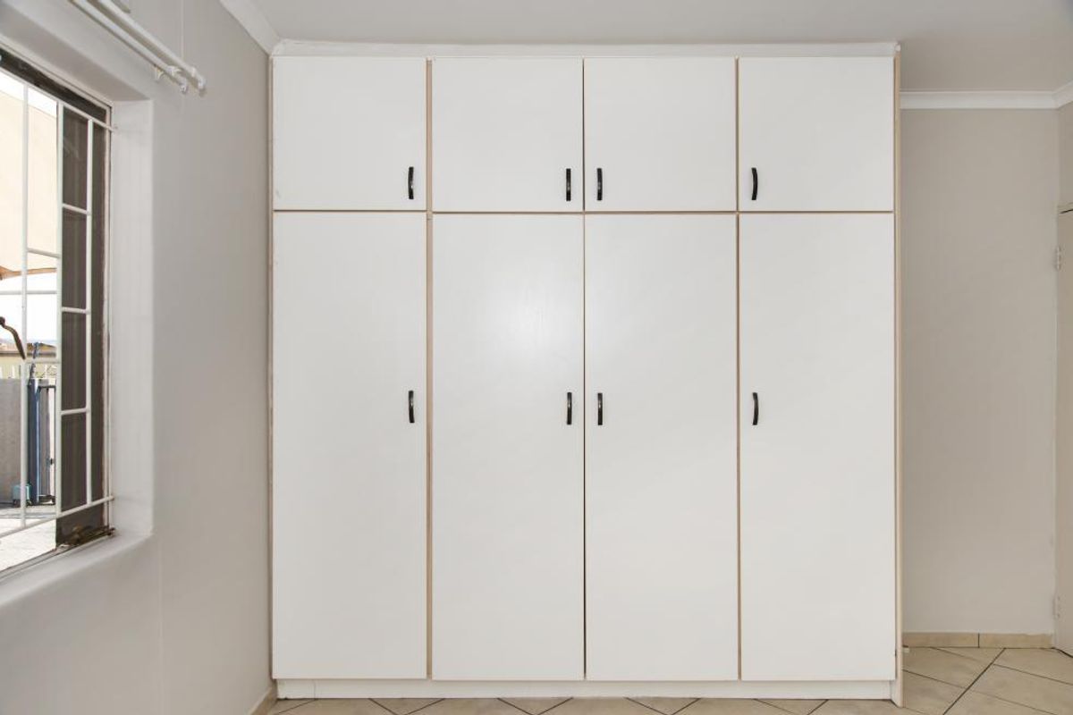 A clean bedroom featuring floor-to-ceiling built-in cupboards, tiled flooring, and a window fitted with security bars.