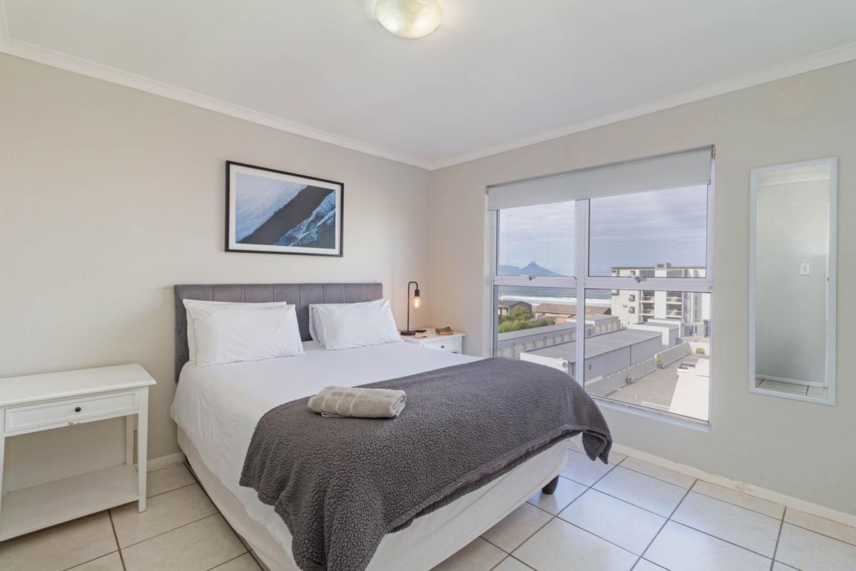 A bright bedroom featuring tiled flooring, a large window with coastal views, and neutral wall finishes.
