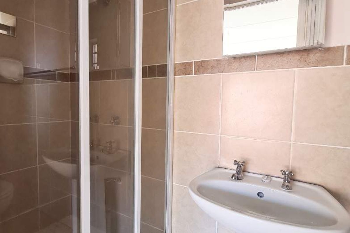 A functional bathroom featuring a pedestal basin, a glass-enclosed shower, and neutral wall tiling.