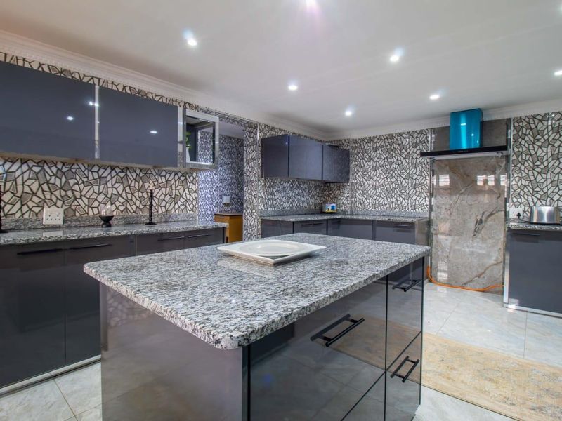 Modern kitchen featuring a central island, granite countertops, high-gloss cabinetry, and a decorative tiled backsplash with integrated extractor fan.