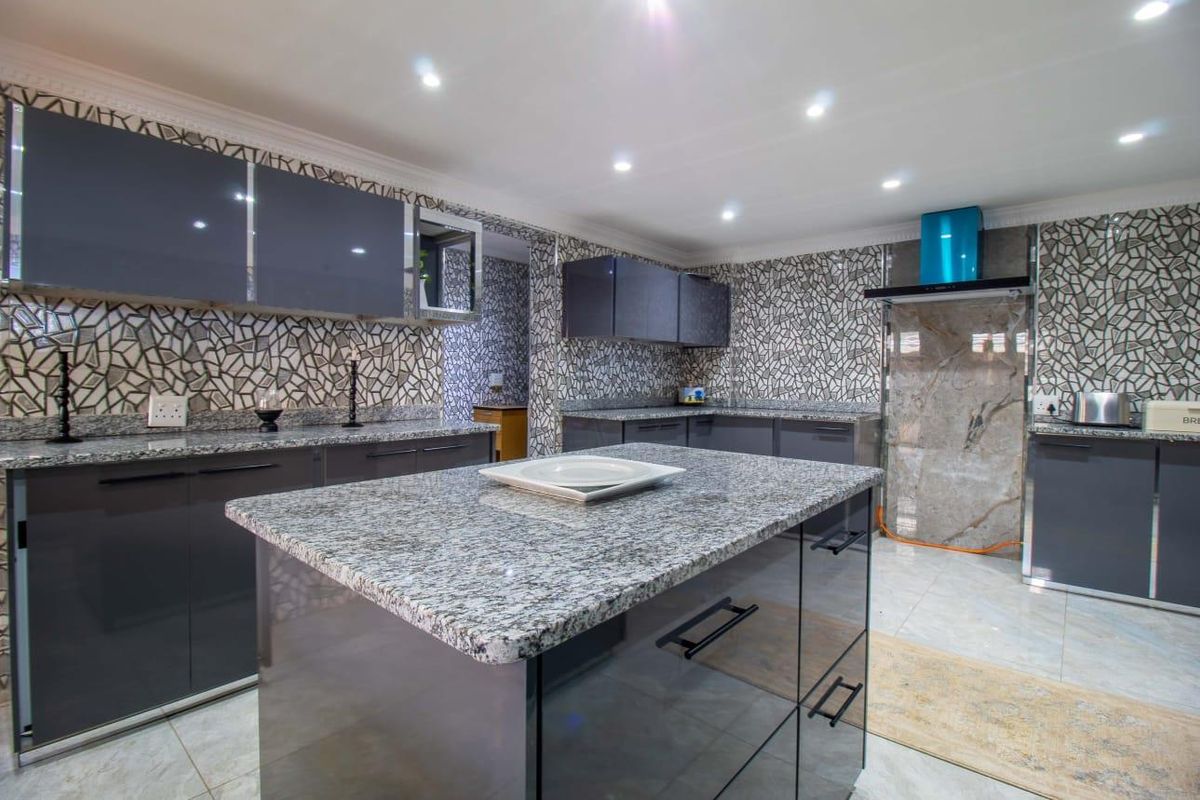Modern kitchen featuring a central island, granite countertops, high-gloss cabinetry, and a decorative tiled backsplash with integrated extractor fan.