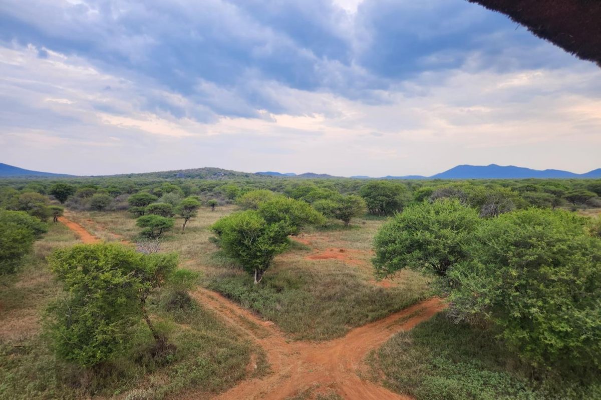 An expansive aerial view of the vacant residential land, featuring natural bushveld vegetation, dirt access tracks, and distant mountain vistas.