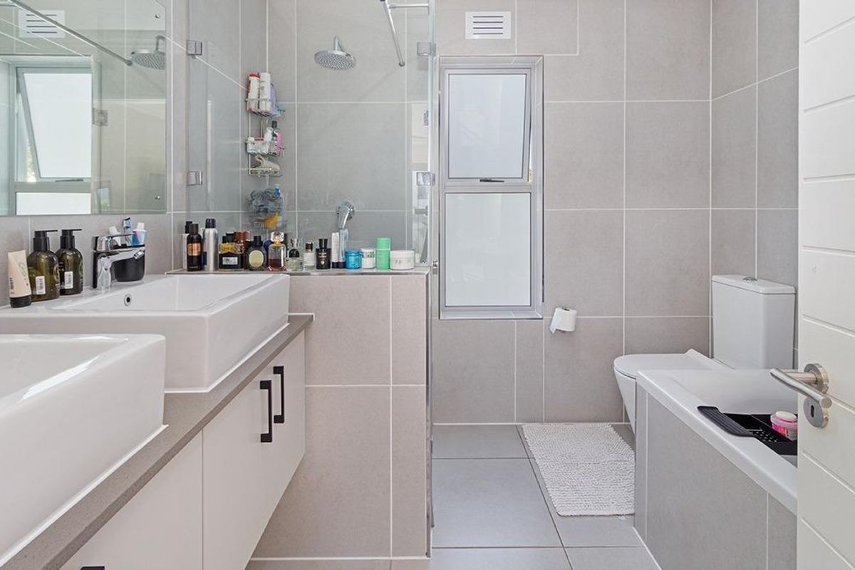 Modern bathroom featuring dual vanity basins, a glass-enclosed shower, and neutral floor-to-ceiling tiling.