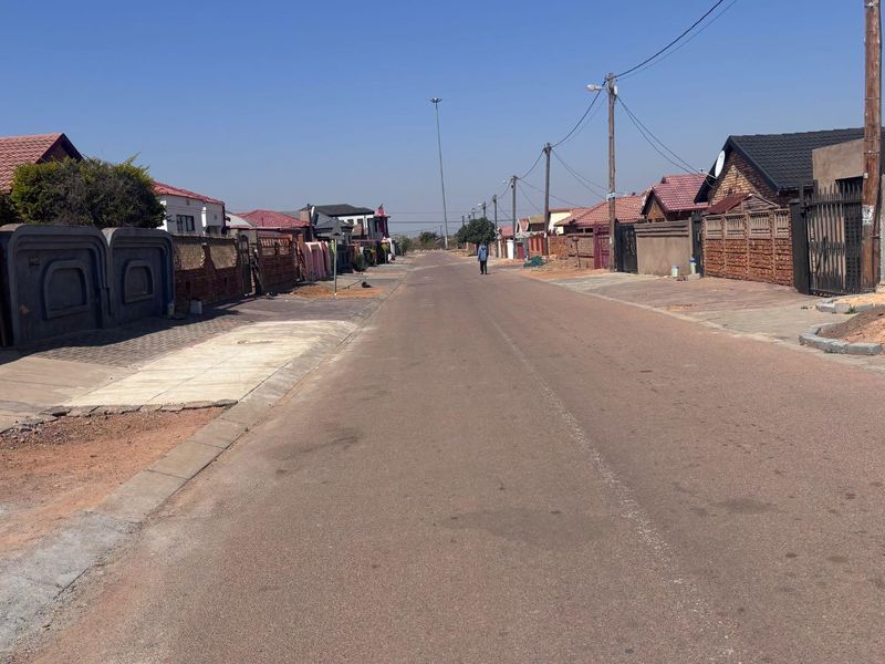 A view of the residential street showing the surrounding neighborhood context, paved road, and boundary walls of the properties.