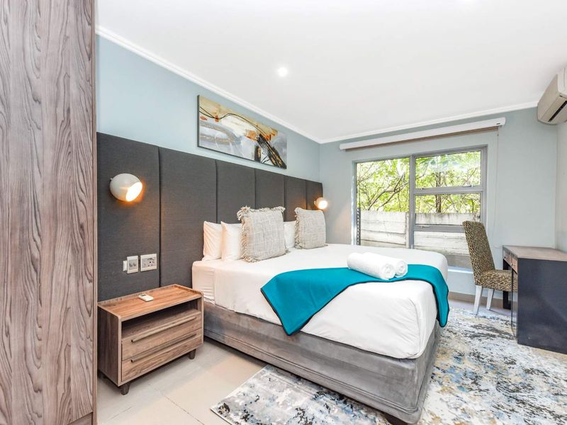 A well-maintained bedroom featuring a large upholstered headboard, built-in wardrobe, split-system air conditioning, and large windows providing natural light.