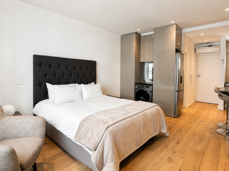 Modern open-plan studio apartment featuring timber flooring, integrated kitchen cabinetry with laundry facilities, and a breakfast bar area.