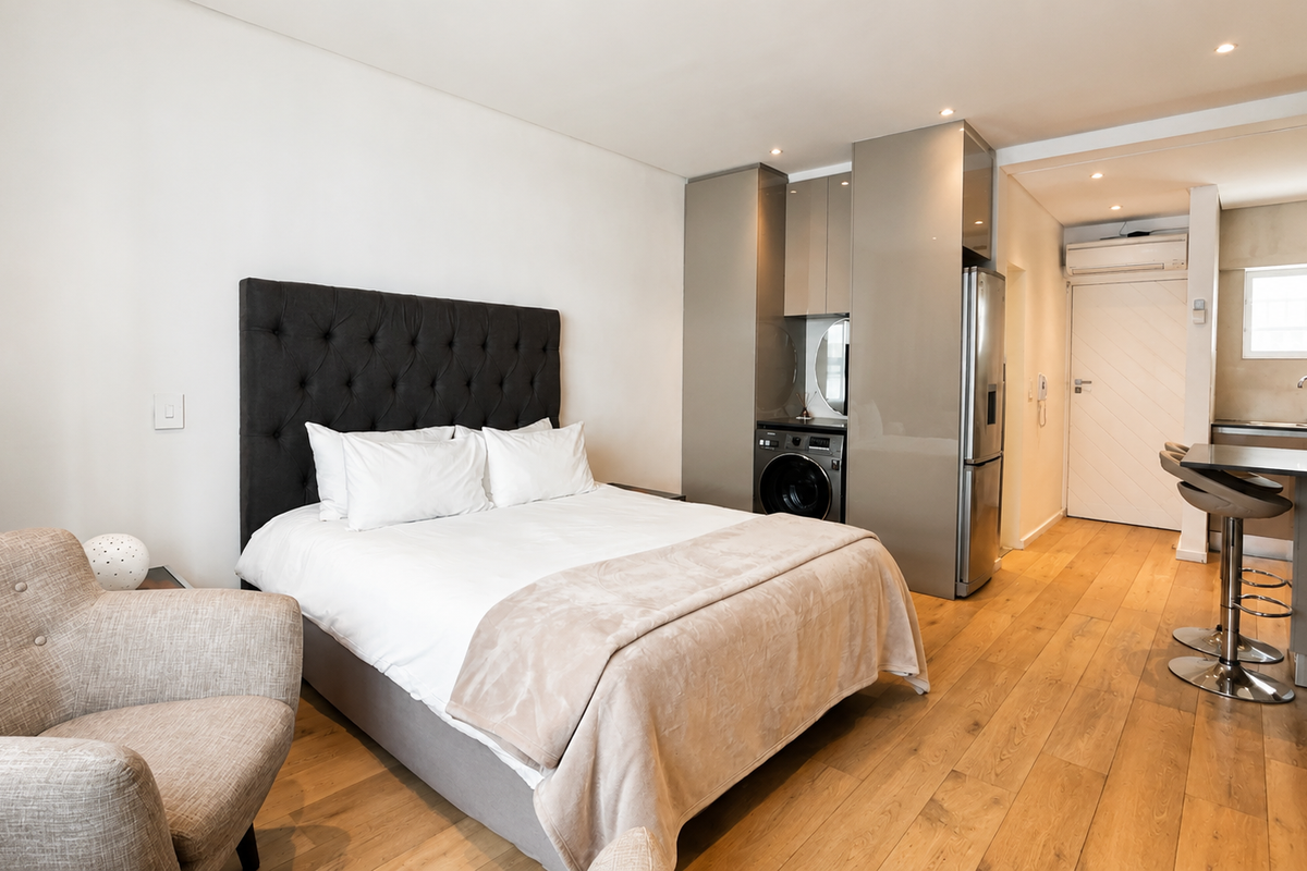Modern open-plan studio apartment featuring timber flooring, integrated kitchen cabinetry with laundry facilities, and a breakfast bar area.