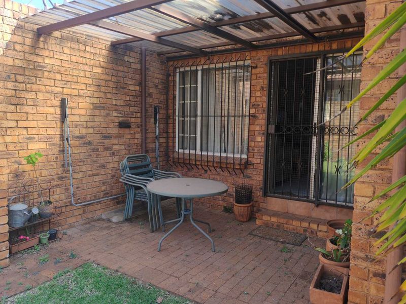 A paved outdoor patio area featuring exposed brick walls, a covered roof structure, and security fixtures, providing a functional space for outdoor relaxation.