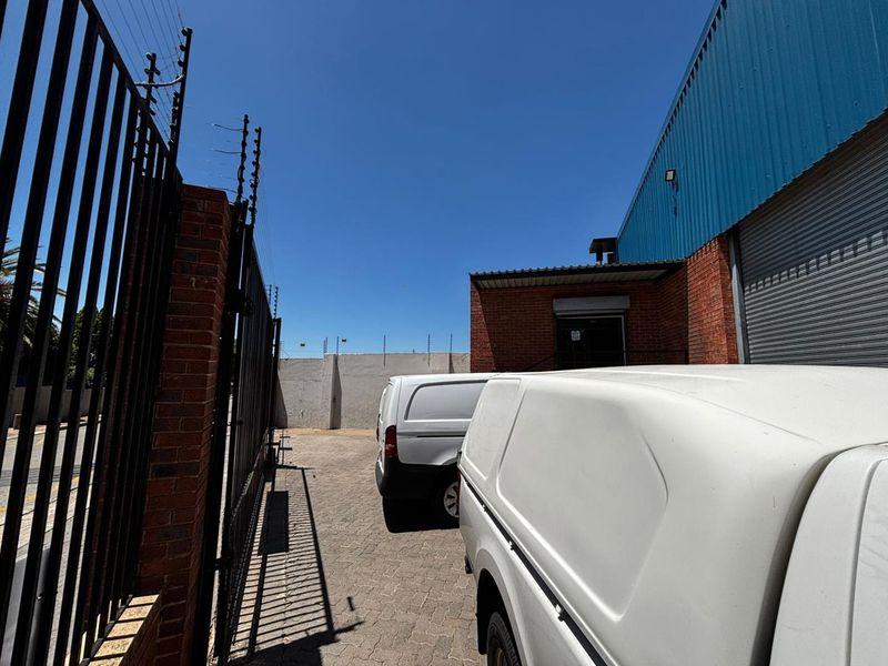 Rear exterior view of a commercial property featuring a paved driveway, brick boundary wall with electric fencing, and a metal roller shutter door.