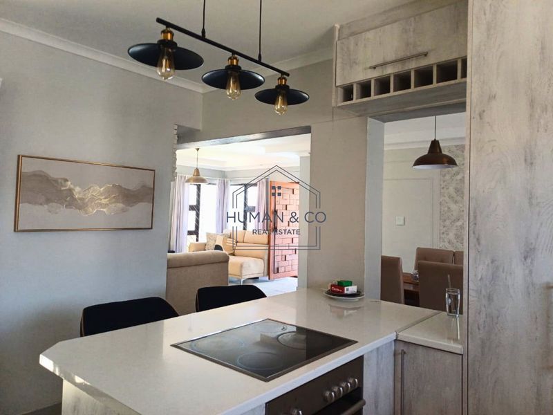 Open plan kitchen area featuring a stone countertop, built-in oven, electric hob, and integrated cabinetry with a wine rack, overlooking the living and dining spaces.