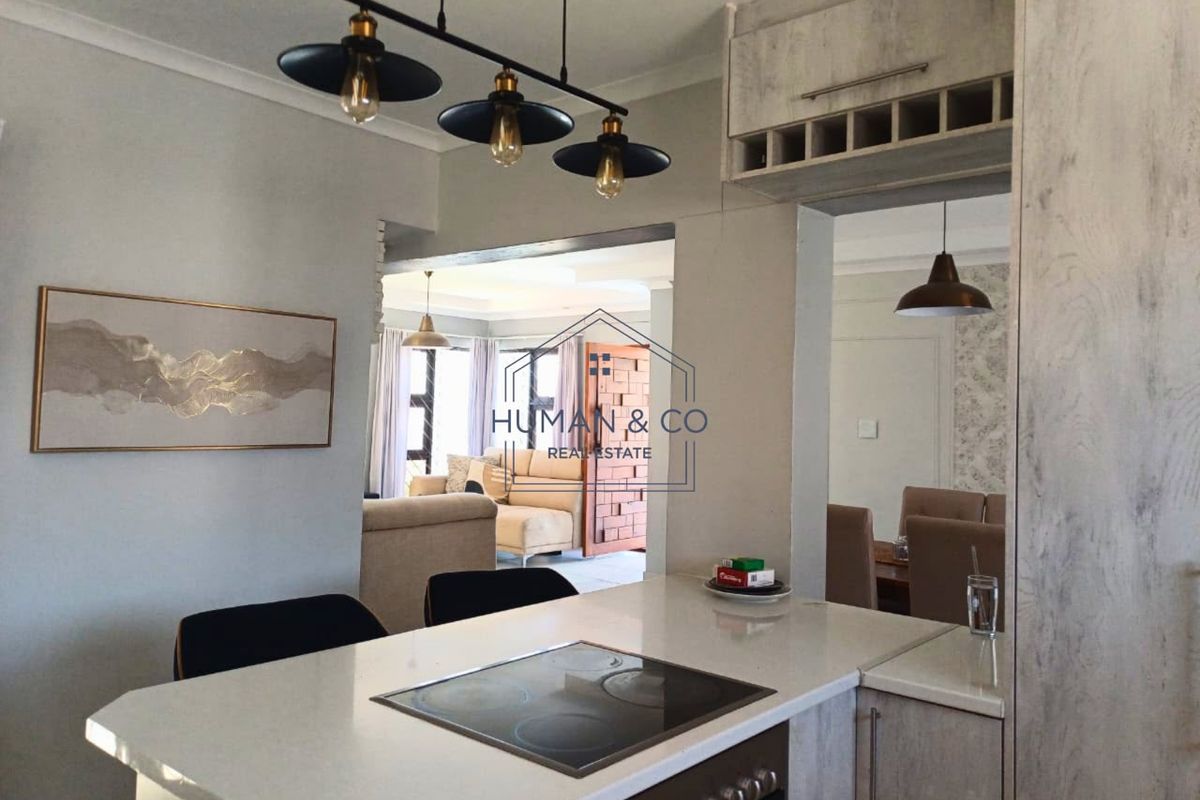 Open plan kitchen area featuring a stone countertop, built-in oven, electric hob, and integrated cabinetry with a wine rack, overlooking the living and dining spaces.