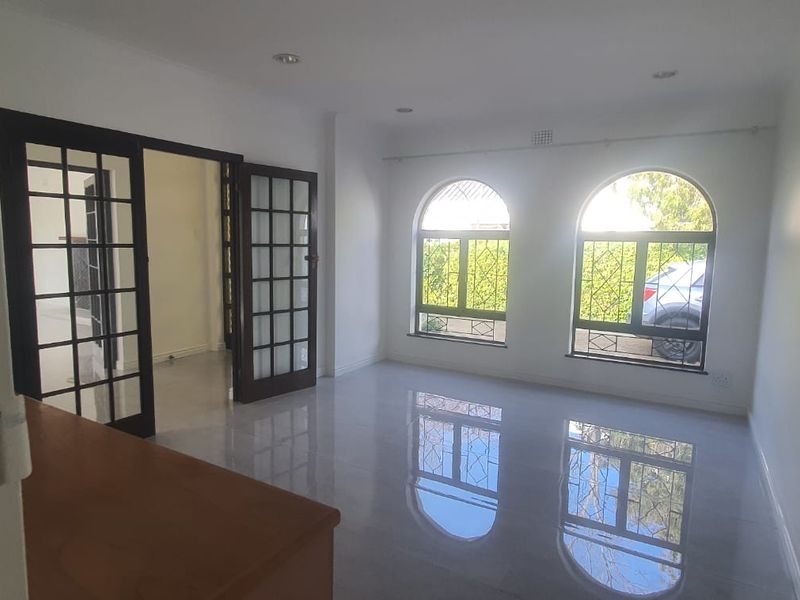 A bright, empty living room featuring polished tiled floors, arched windows with security bars, and elegant French doors leading to an adjacent space.