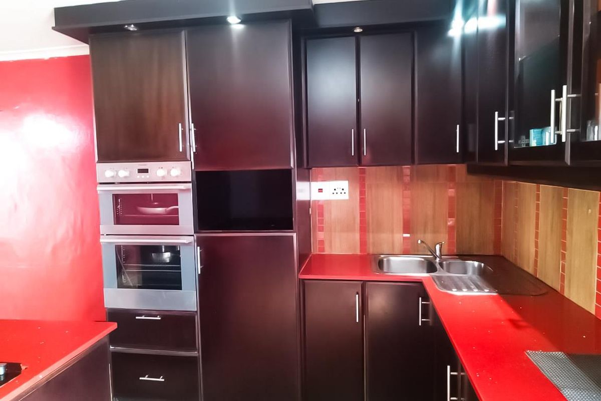 A functional kitchen featuring dark wood cabinetry, a built-in oven and microwave, red countertops, and a double sink with tiled backsplash.