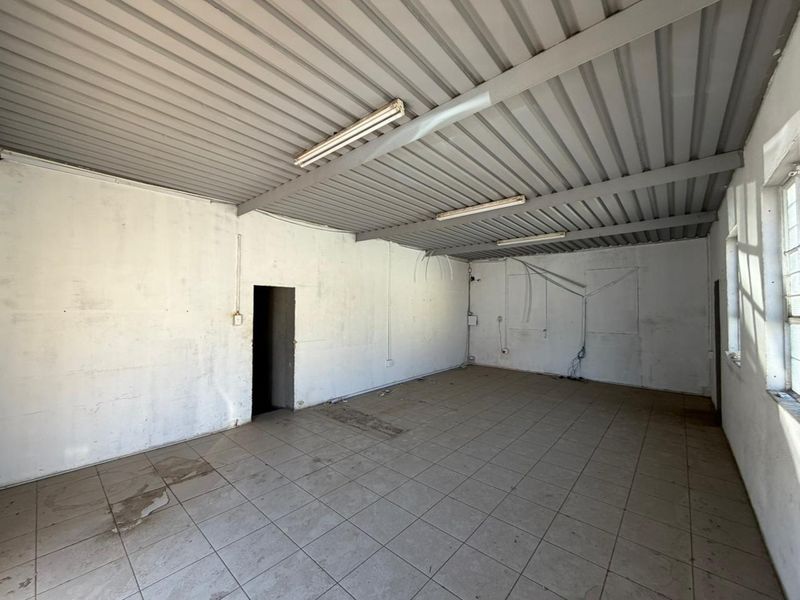 An empty, industrial-style utility space featuring exposed metal ceiling, fluorescent lighting, and tiled flooring, suitable for storage or workshop use.