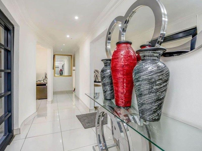 A bright and modern hallway featuring polished tiled flooring, recessed downlighting, and elegant coved cornicing, leading through to adjacent living spaces.