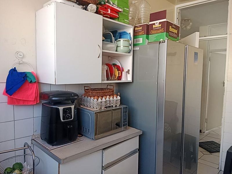 A compact kitchen area featuring built-in cabinetry, tiled backsplash, and tiled flooring, offering functional storage space for daily culinary needs.