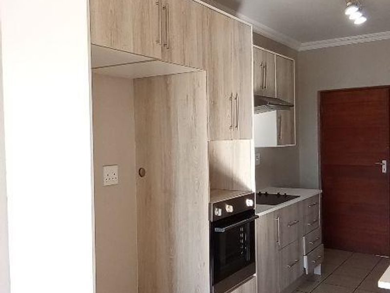 A functional kitchen featuring light wood-grain cabinetry, built-in oven and hob, extractor fan, and neutral tiled flooring.