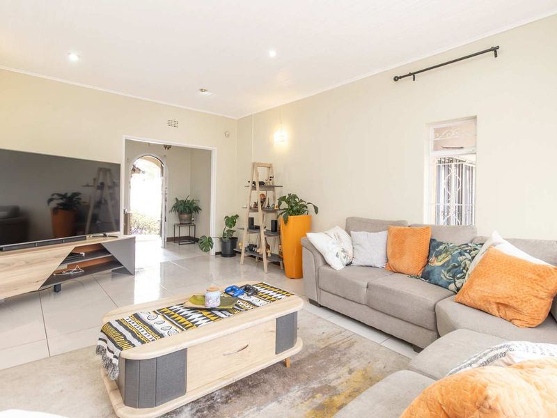A bright and spacious living room featuring neutral tiled flooring, recessed downlighting, and an open-plan layout leading to an arched entryway.